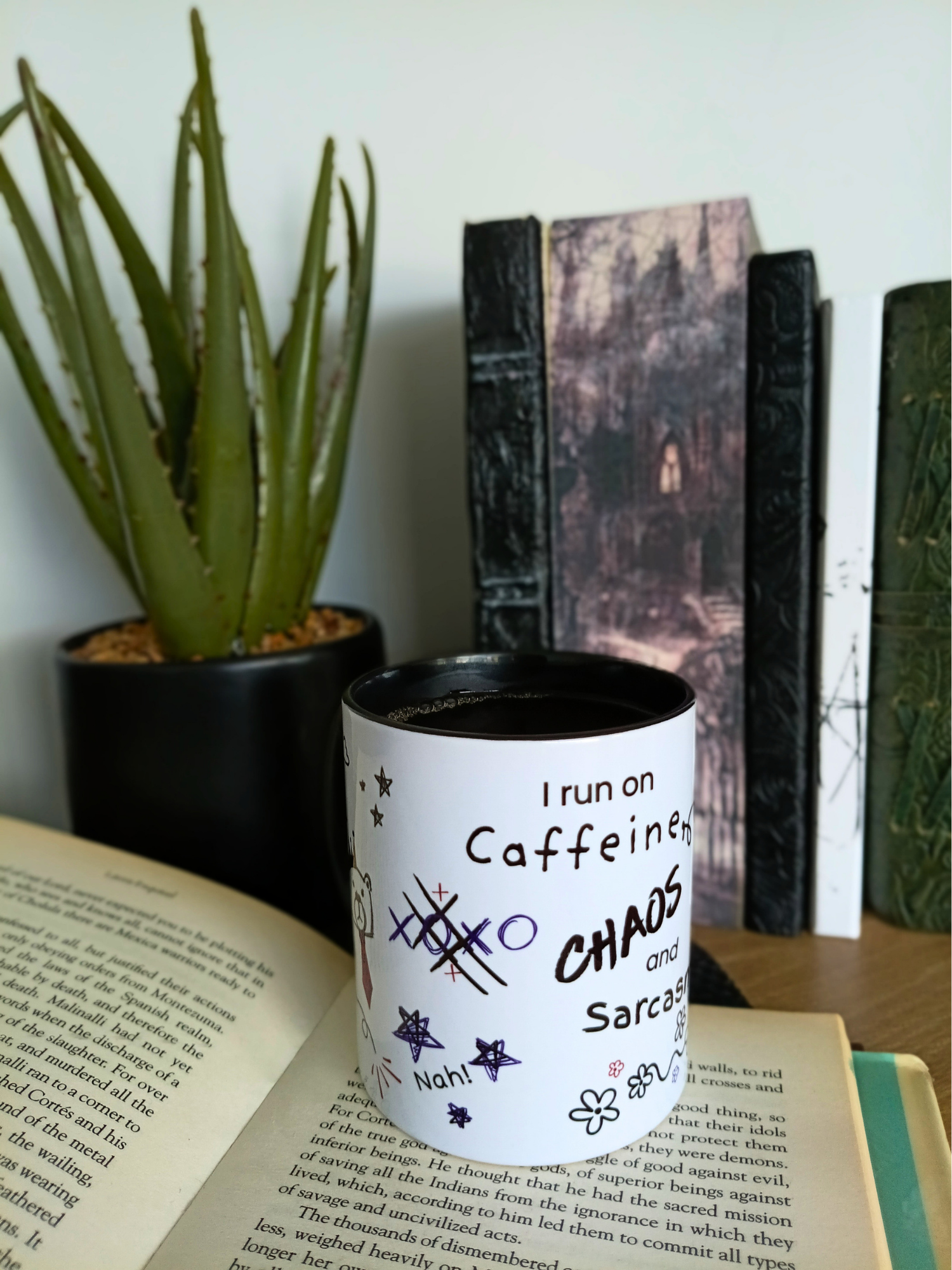 White mug with text on a book next to a plant and books