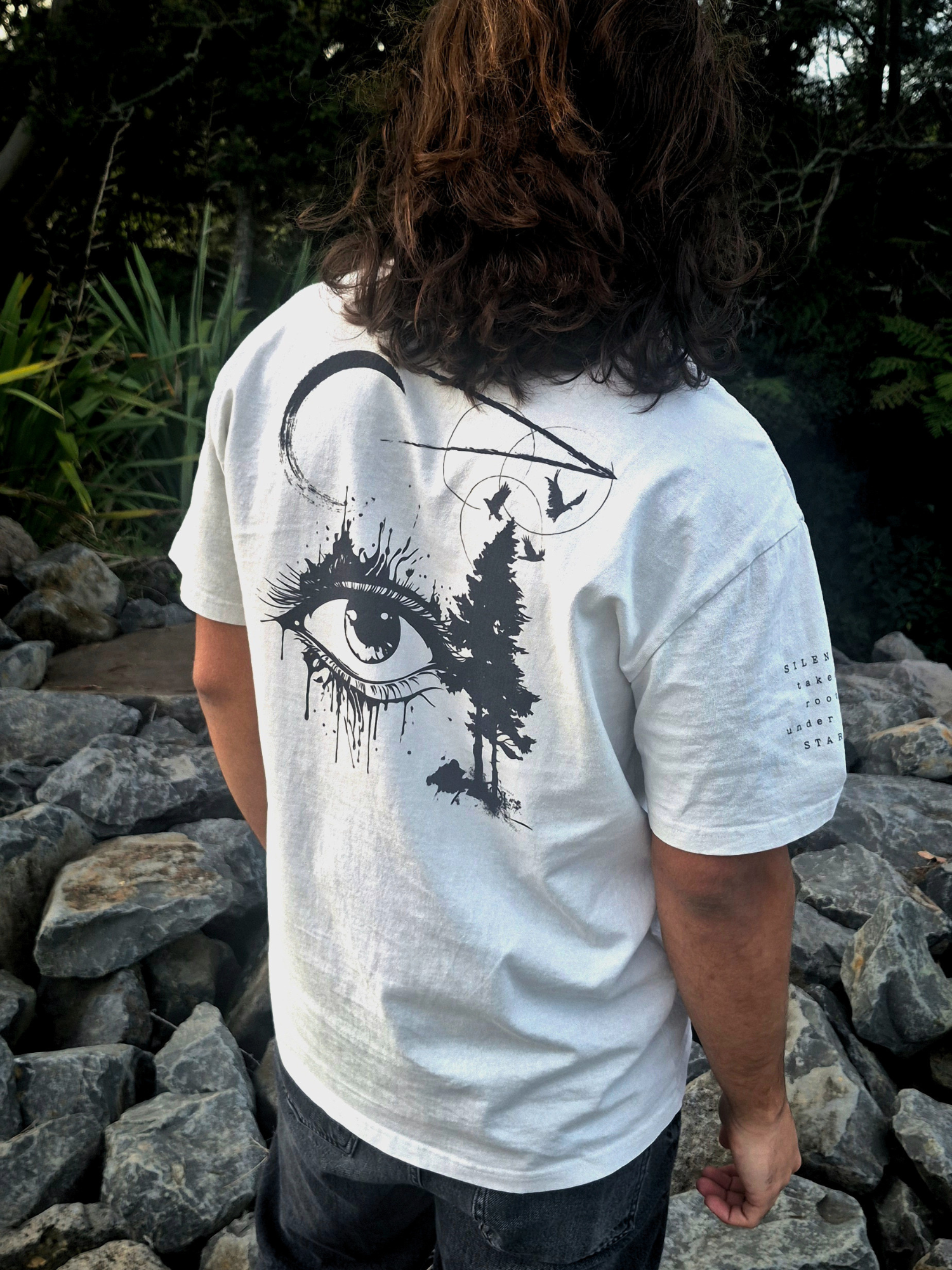 Person wearing a white t-shirt with a black eye design outdoors.