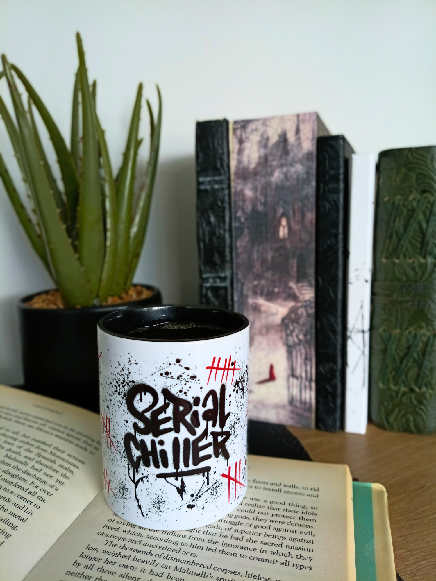 Cup with 'Serial Chiller' design on a book next to a plant and decorative items.