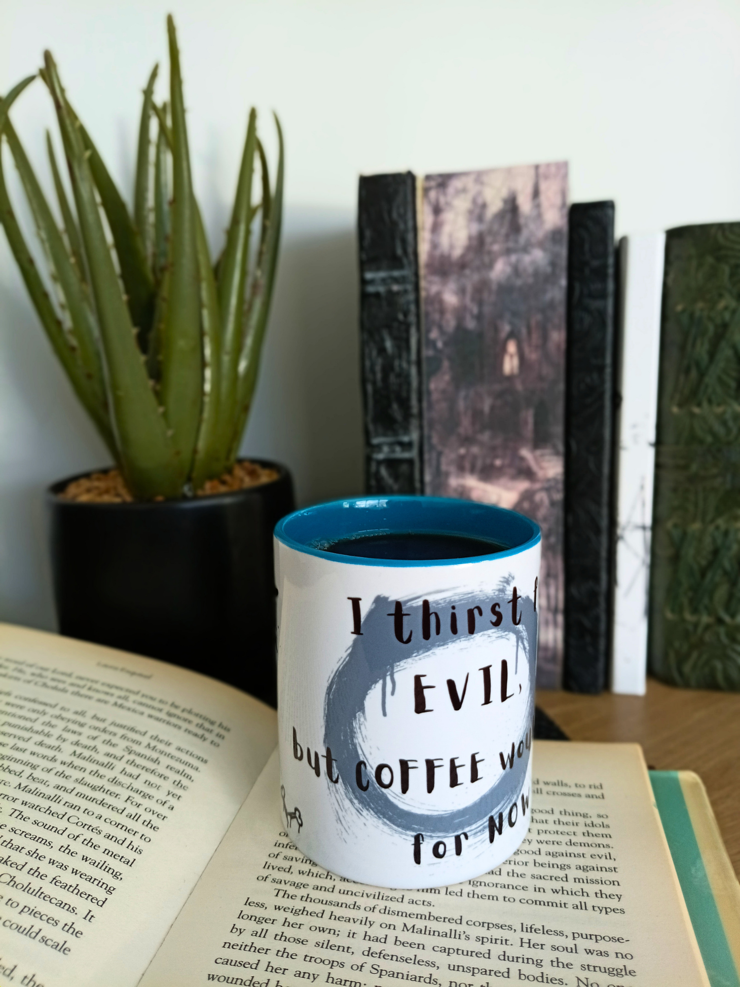 Mug with text on a table next to an open book and plants